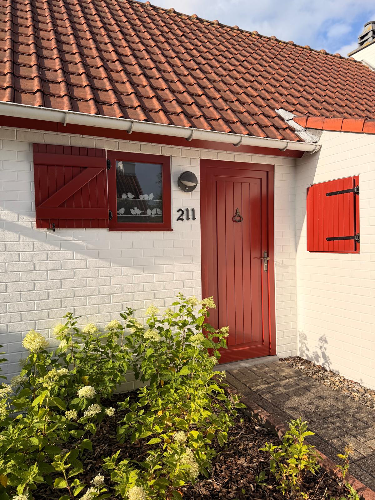 Red front door and flowering garden border at NordHuys